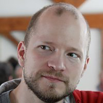 A photographic portrait shows a figure with light skin, brown beard, balding head, and dark eyes gaze to the left and smile slightly.