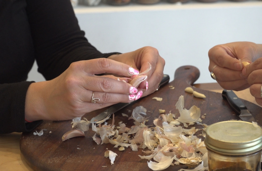 A woman's hands peel garlic on the kitchen counter.