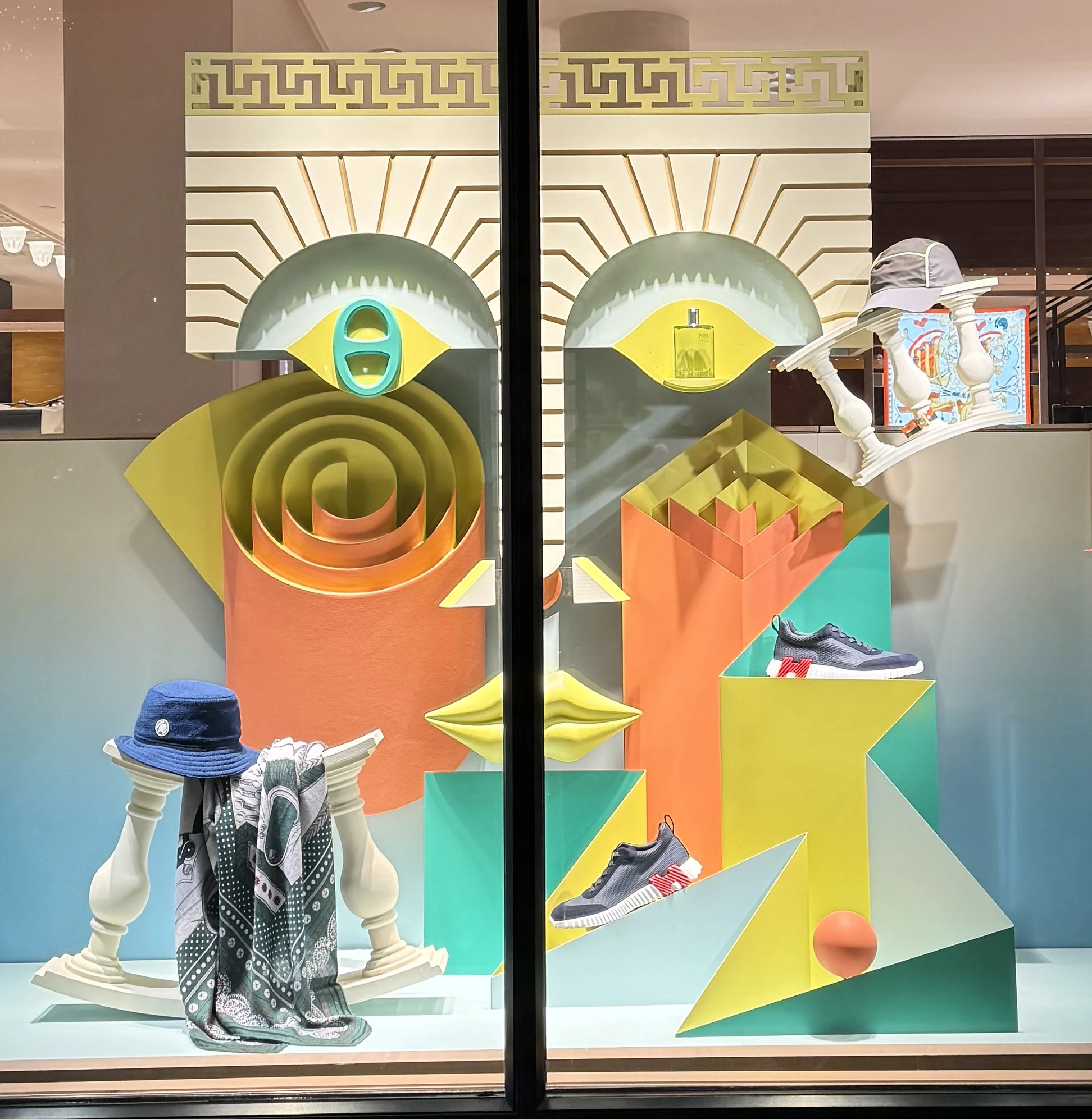 A window display of the Hermes storefront. In it, colorful 3D geometric shapes and pillars are arranged in a way to look like a face. Sneakers and ties are also artfully arranged across the display.